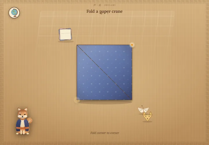 Folding a paper crane in Atlas Jr: a square of origami paper folded corner to corner on a tatami mat, with a shiba inu looking on.